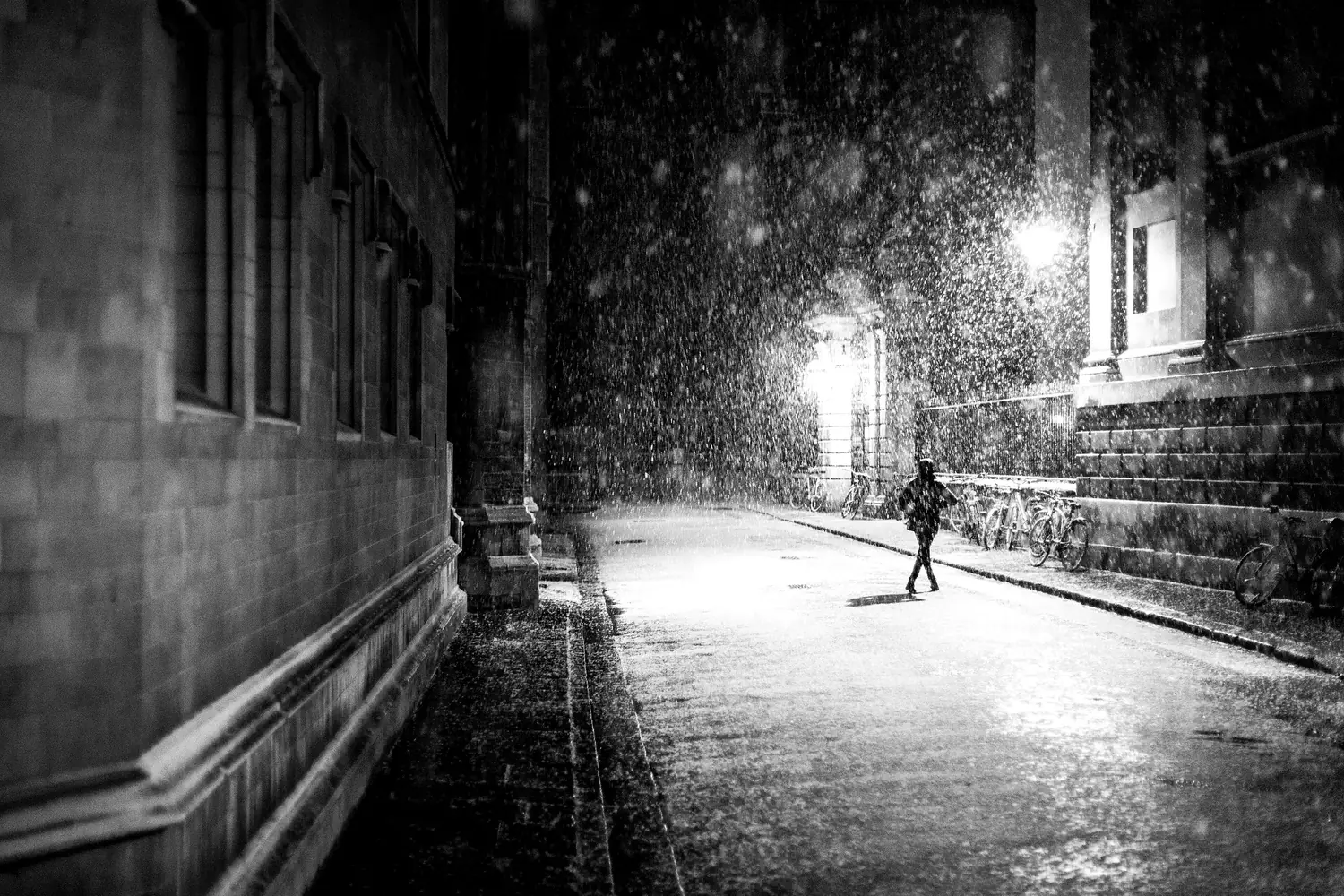Una persona corre di notte sotto la pioggia in un vicolo vuoto