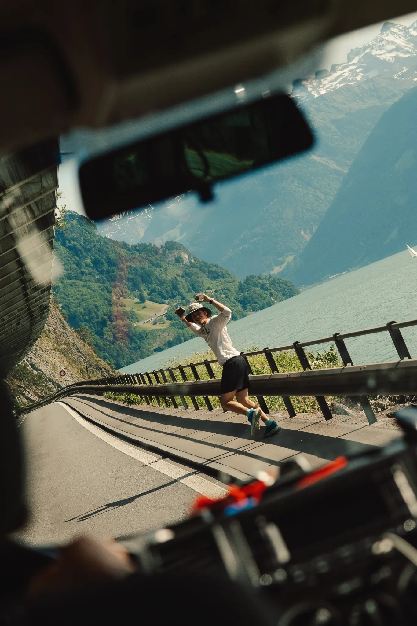 Una persona corre sull'Axenstrasse, vista attraverso il parabrezza dell'auto di supporto. Dietro, il lago d'Uri.